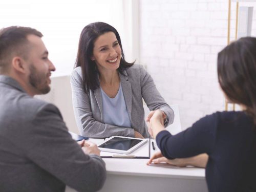 Deal. Positive insurance broker handshaking with young couple after signing agreement contract
