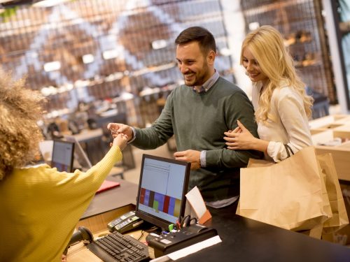 Handsome young couple paying female sales assistant with credit card in clothes shop